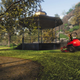Cutting grass in a riding mower near a gazebo.